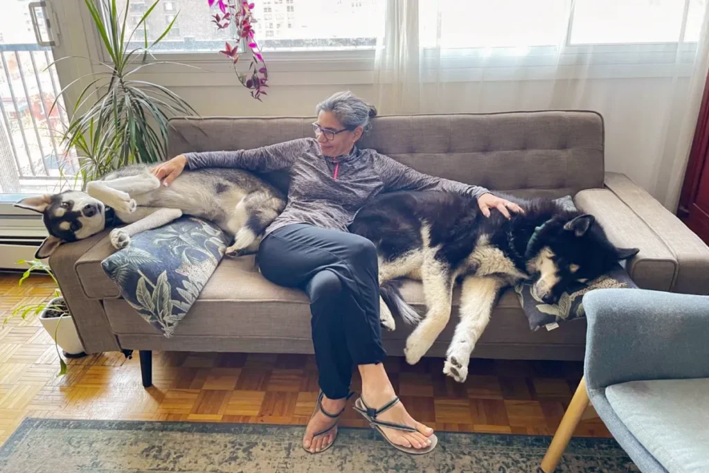 Qué es el housesitting: mujer descansando en un sofá con dos perros durante una experiencia de housesitting en una casa